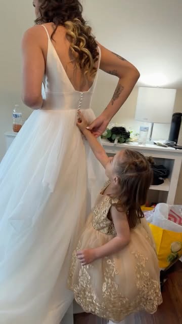 A young girl helping fasten a bride’s wedding dress
